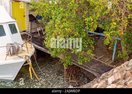 Una barca ormeggiata accanto a un molo vecchio con una passeggiata tra gli alberi e sporchi acqua vorticoso al di sotto di Foto Stock