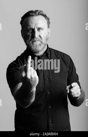 Arrabbiato maturo uomo barbuto con la mano di tatuaggi che mostra il dito medio Foto Stock
