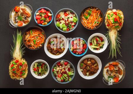 Assortimento di Thai piatti cotti in recipienti su un calcestruzzo nero lo sfondo. Vista dall'alto. Foto Stock