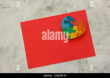 Multicolore in legno puzzle a forma di cuore su un foglio di colore rosso su sfondo grigio Foto Stock