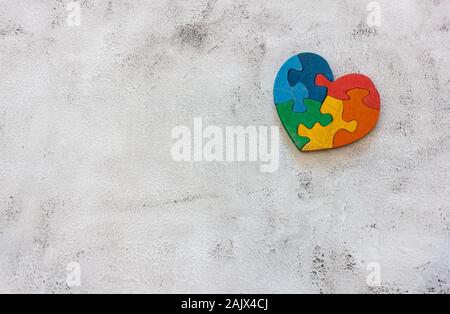 Multicolore in legno puzzle a forma di cuore su uno sfondo grigio. Concetto il giorno di san valentino, relazione. Foto Stock