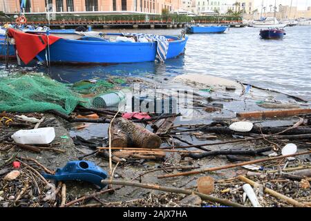 Plastica e microplastic rifiuti ed immondizia galleggiante in acqua con rete da pesca e la barca di legno su sfondo. Oceano Mare e inquinamento in plastica Foto Stock