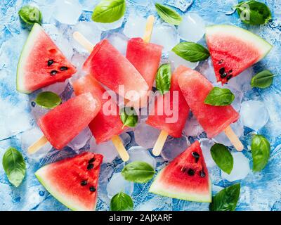 Vista dall'alto di cocomero e basilico popsicles su sfondo blu con fresco verde foglie di basilico e fette di anguria. Ricetta Popsicles idea. Foto Stock