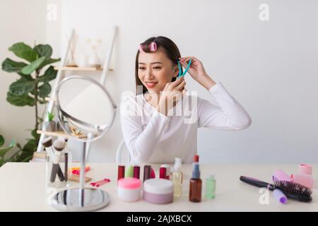 Tutorial di acconciatura. Donna asiatica spazzolare i capelli e sorridente piacevolmente durante le riprese di un tutorial per la sua bellezza blog Foto Stock