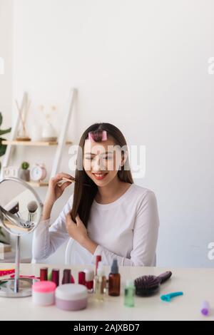 Tutorial di acconciatura. Donna asiatica spazzolare i capelli e sorridente piacevolmente durante le riprese di un tutorial per la sua bellezza blog Foto Stock