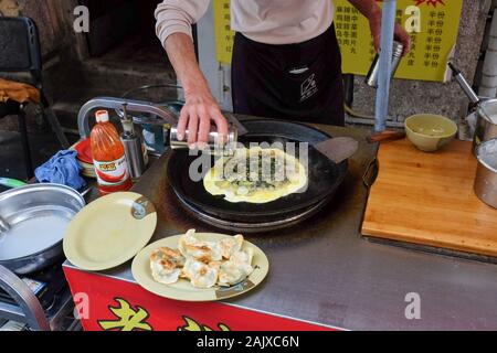 Un uomo cucina il cibo in una stalla di strada sull'isola di Gulangyu a Xiamen (Amoy), Cina. Foto Stock