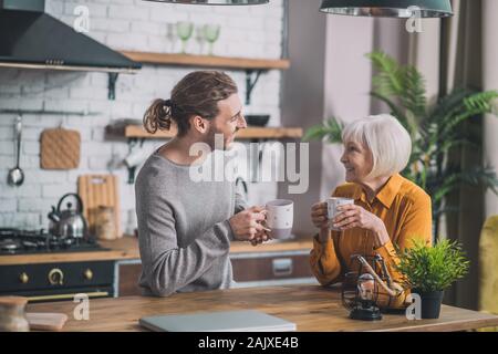 Grey-haired mom e suo figlio seduto in cucina Foto Stock