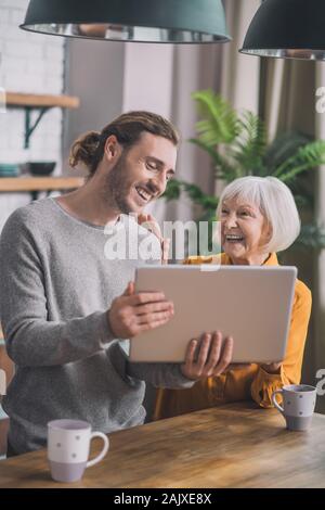 Grey-haired mom e suo figlio a discutere di qualcosa di vivo in cucina Foto Stock