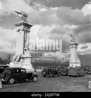 1950s, storico, Parigi, Francia, automobili dell'epoca passando le due colonne di pietra con sculture. Foto Stock