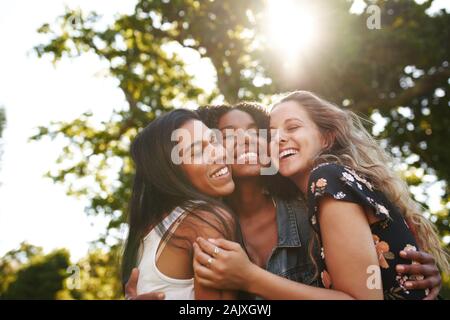 Ritratto di un felice gruppo multietnico amiche abbracciando e abbracciare ogni altra ridere e divertimento all'aperto in un parco Foto Stock