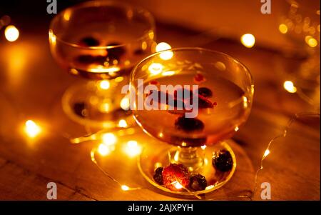 Due bicchieri da cocktail con bacche e luci incandescente su sfondo in legno ancora vita Foto Stock