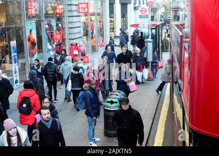 Christmas Shopper in abbigliamento invernale in piedi in attesa di un autobus alla fermata fuori Uniqlo store in Oxford Street Londra Inghilterra KATHY DEWITT Foto Stock