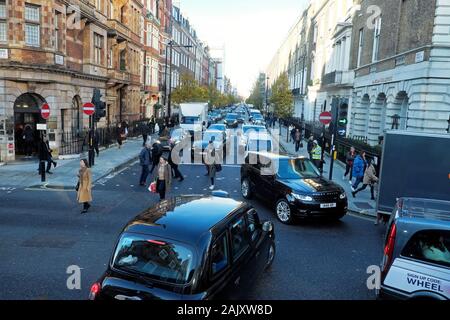 Vista di Harley Street del traffico taxi, auto, pedoni persone attraversando road sistema a senso unico in Marylebone Londra Ovest Inghilterra UK KATHY DEWITT Foto Stock