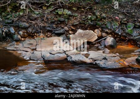 Pietra arenaria nel letto del fiume Don, con acqua che scorre rapidamente attraverso antichi boschi, e l'ocra trafilare dalle vicine giacche di carbone Foto Stock