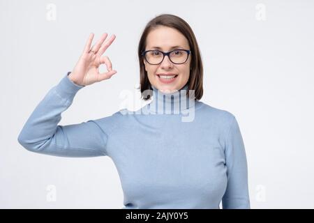 Caucasian donna matura con un ampio sorriso che indossano occhiali che mostra il simbolo ok con le dita. Il linguaggio del corpo okay significato super gesto per il negozio ottica, de Foto Stock