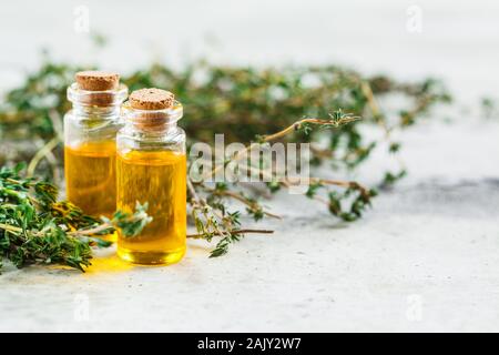 Olio essenziale di timo in bottiglie di vetro, uno sfondo grigio. Foto Stock