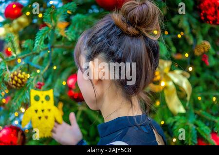 Giovane donna femmina lady guardando ornamento di Natale appeso su albero in mezzo ad altri addobbi e luci all'interno della cupola di fiori dei giardini Foto Stock