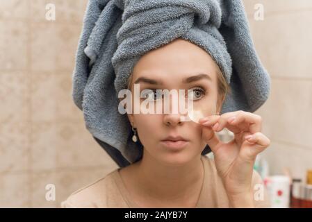 Una bellissima ragazza con un asciugamano sul suo capo bastoni patch di idrogel sotto i suoi occhi sul suo viso. La ragazza si prende cura per la pelle e la idrata la zona aro Foto Stock