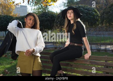 Ritratto di due belle generazione messicano ragazze. Una ragazza in un cappello nero si trova sul retro di un sedile a panchina, accanto a una ragazza con i capelli ricci e un bianco swea Foto Stock