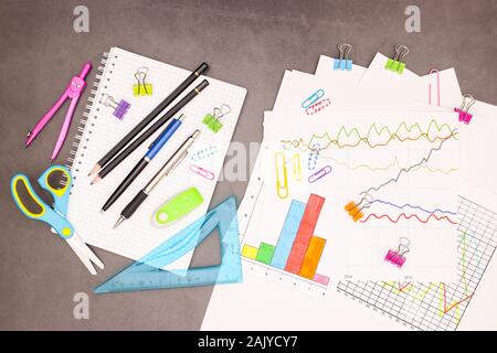 Lap top, statistiche dei piani e delle forniture di ufficio su sfondo grigio Foto Stock