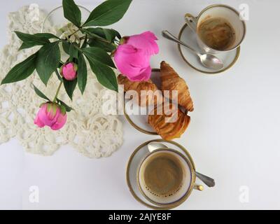La prima colazione con 2 tazza di caffè e croissant, bouquet di fiori di colore rosa peonie, vista dall'alto Foto Stock