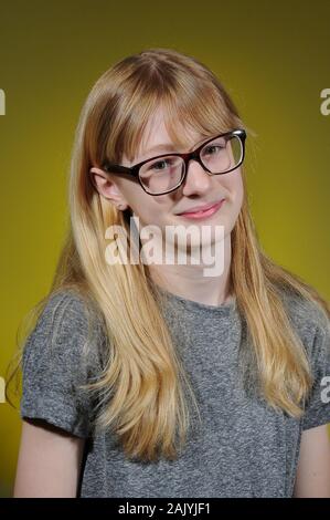 Bella bionda ragazza vestita di nero occhiali incorniciati e grigio di una t-shirt isolate su un sfondo graduata Foto Stock