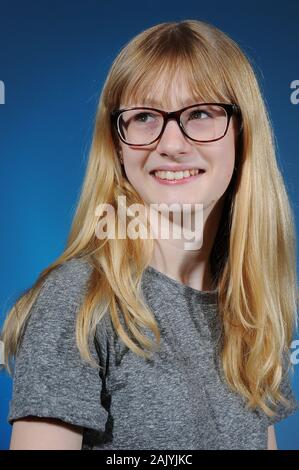 Bella bionda ragazza vestita di nero occhiali incorniciati e grigio di una t-shirt isolate su un sfondo graduata Foto Stock