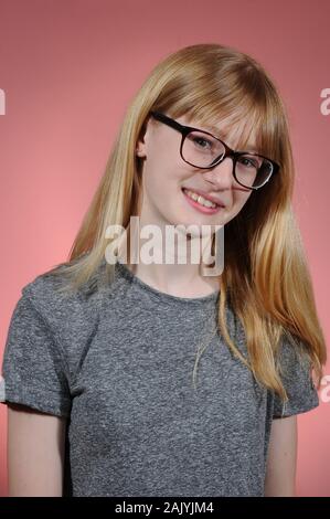 Bella bionda ragazza vestita di nero occhiali incorniciati e grigio di una t-shirt isolate su un sfondo graduata Foto Stock