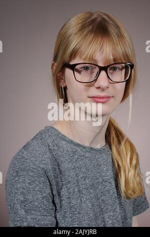 Bella bionda ragazza vestita di nero occhiali incorniciati e grigio di una t-shirt isolate su un sfondo graduata Foto Stock