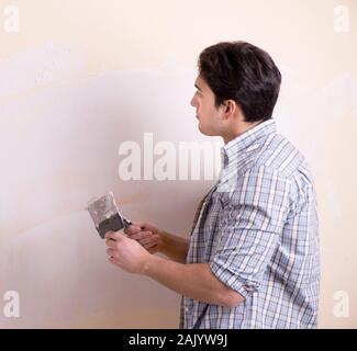 Il giovane uomo applicando intonaco sulla parete di casa Foto Stock