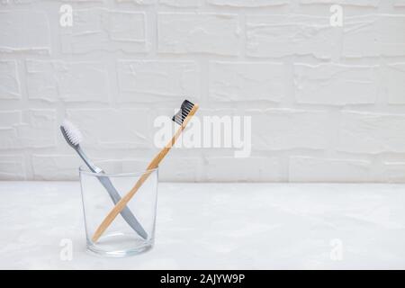 Spazzolino da denti in plastica e eco-friendly bamboo spazzolino da denti in un bicchiere di vetro grigio su sfondo neutro Foto Stock