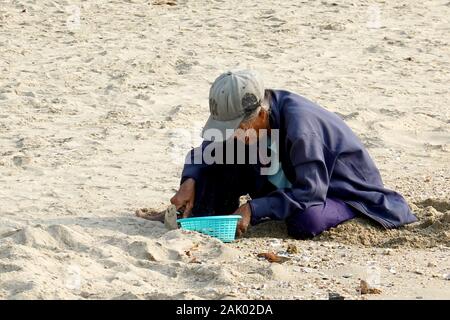 Il sambuco donna seduta sulla spiaggia e cercando di trovare le vongole. Foto Stock