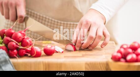 Donna affettamento rafano fresco a casa in cucina Foto Stock