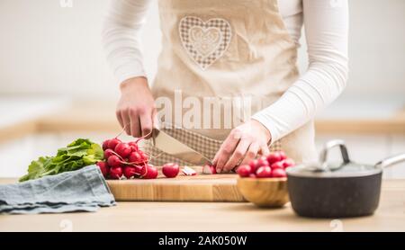 Donna affettamento rafano fresco a casa in cucina Foto Stock