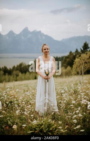 Sposa in campo di fiori selvatici in Wyoming tiene bouquet di fiori. Foto Stock