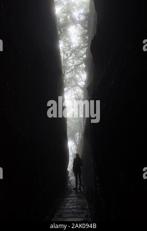 Silhouette di un alto irriconoscibile donna come lei si affaccia da una drammatica spaccatura fra le rocce dei monti dell'isola di Madeira. Foto Stock