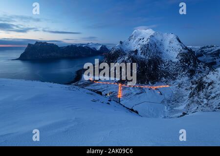 Streelights del villaggio di Uttakleiv brillare sotto Himmeltindan picchi di montagna in inverno crepuscolo, Vestvågøy, Isole Lofoten in Norvegia Foto Stock