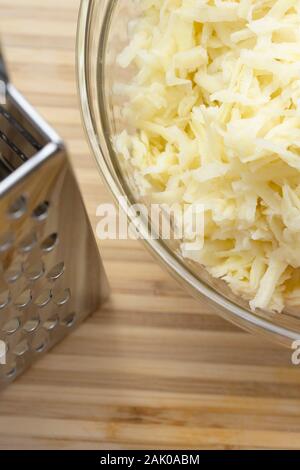 Primo piano ad angolo elevato di patate grattugiate in una ciotola di vetro accanto al grattatore Foto Stock