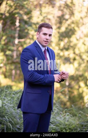 Un giovane uomo sicuro sorride alla macchina fotografica mentre si sta all'esterno. Foto Stock