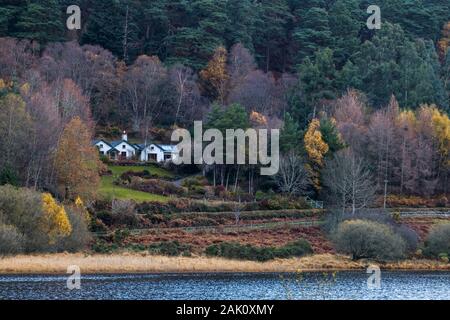 Un cottage bianco si trova tra una foresta autunnale e il lago superiore di Glendalough nel parco nazionale delle montagne di Wicklow in Irlanda. Foto Stock