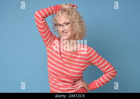 Attraente sorridente caucasica donna matura con capelli biondi in abiti a righe isolate su parete blu. Studio shot Foto Stock