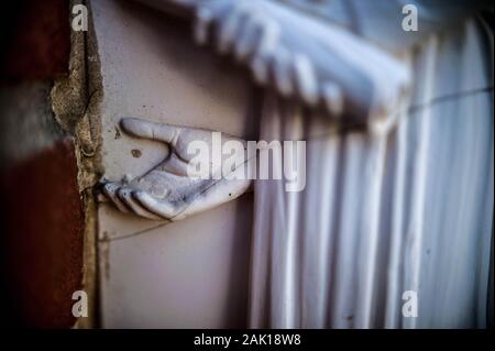 Una mano di pietra su una statua incrinato raggiunge fuori da dietro una figura umana Foto Stock