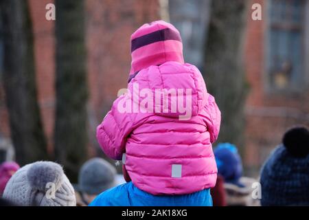 Un bambino piccolo in vestiti caldi si siede sul suo padre il collo. Camminando sulla strada. Close up. Foto Stock