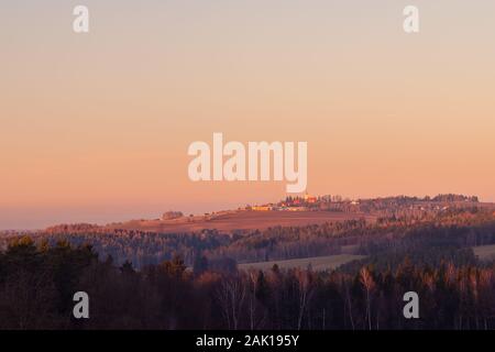 tramonto sul paesaggio rurale con villaggio - nella foresta in primo piano, all'orizzonte sulla collina chiesa e diversi edifici, colore arancione cielo Foto Stock