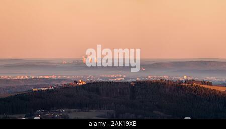 Paesaggio - foresta e collina con la chiesa in primo piano, la città sullo sfondo e le centrali nucleari camini (Temelin, Cechia) all'orizzonte Foto Stock