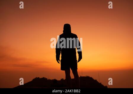 Silhouette di un uomo da dietro, sorge sulla sommità di una collina / montagna guardando un bellissimo tramonto. RF concettuale di ispirazione foto motivazionale Foto Stock