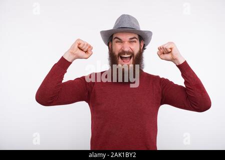 Ritratto di stupito uomo barbuto in grey hat celebrando la vittoria Foto Stock