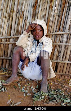 Un ragazzo africano seduto sul pavimento accanto a una recinzione Foto Stock