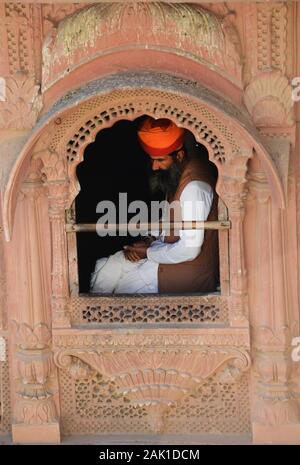 Un uomo di Rajasthani seduto da una finestra di palazzo al forte di mehrangarh in Jodhpur, India. Foto Stock