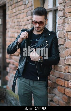 Hipster Man con occhiali da sole in una giacca in piedi da un muro di mattoni. Foto Stock